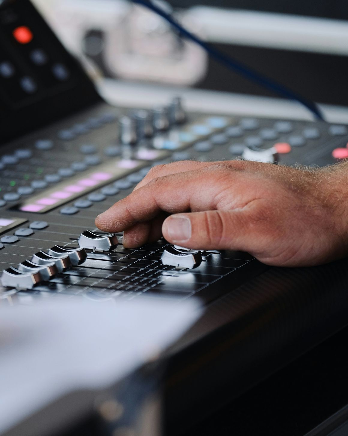 A hand adjusting faders on a mixing console.
